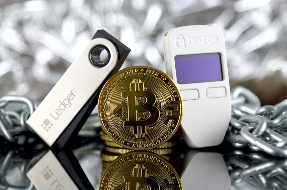 Ledger and Trezor hardware wallets next to a physical Bitcoin token