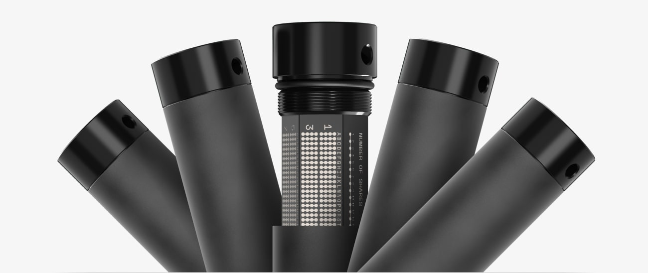 Five metal seed backup capsules fanned out, the centre one open to show engraved letter tiles and a share-number dial
