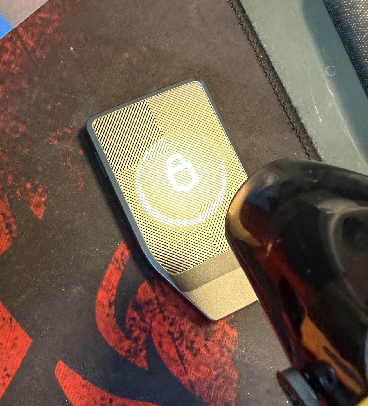 A sealed Trezor Safe 7 face down on the bench with a heat gun nozzle held over its patterned rear panel and plastic opening cards beside it