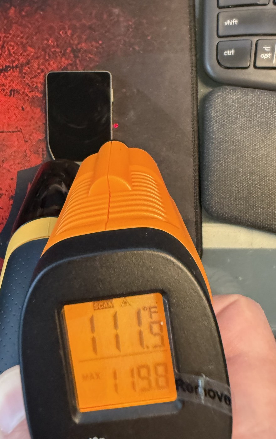 Infrared thermometer aimed at the sealed Trezor Safe 7, laser dot on the glass, reading 111.9 F with a session maximum of 119.8 F