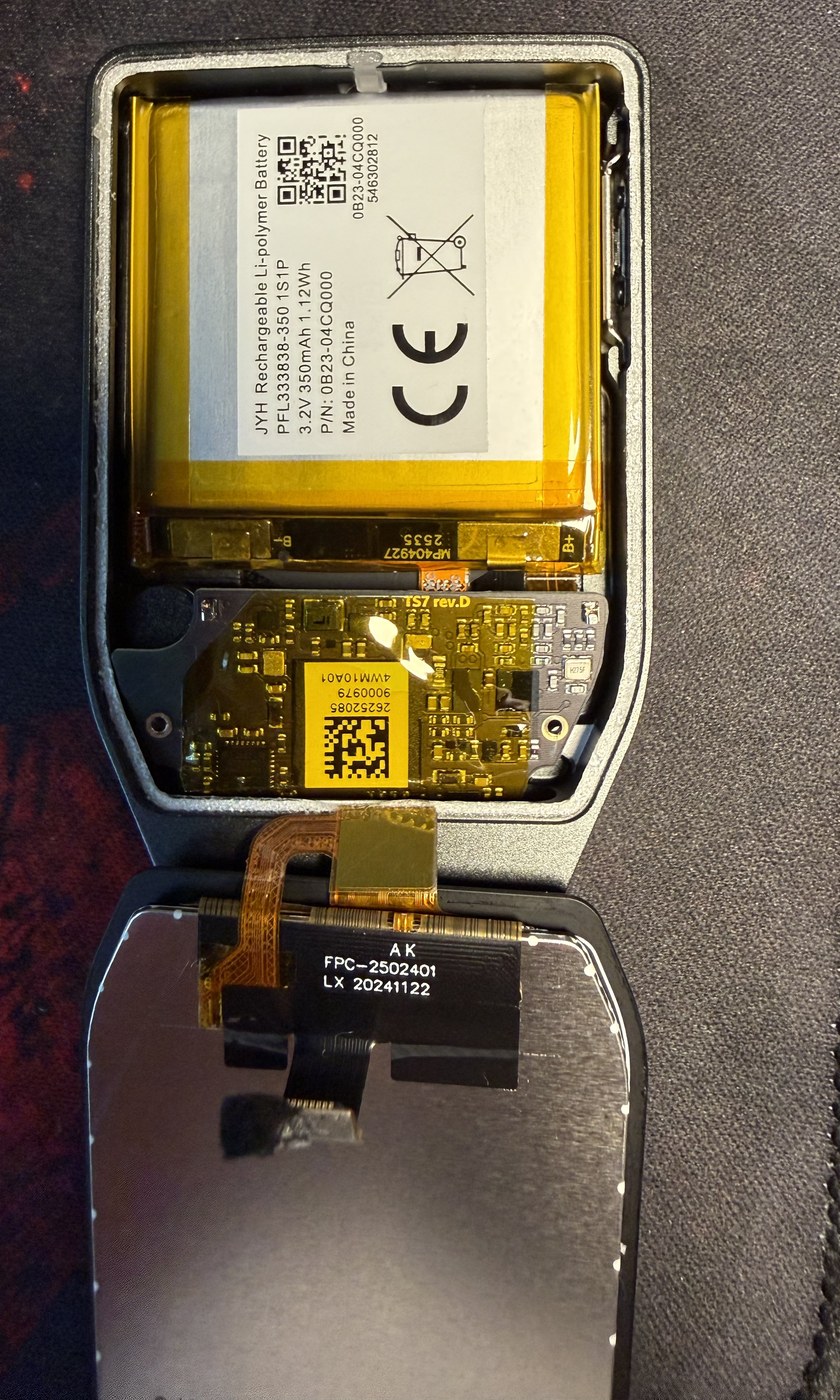 Inside the Trezor Safe 7: the 350 mAh lithium polymer battery fills the upper enclosure, the TS7 rev.D mainboard with its USB-C port sits at the narrow end, and the display is folded out below