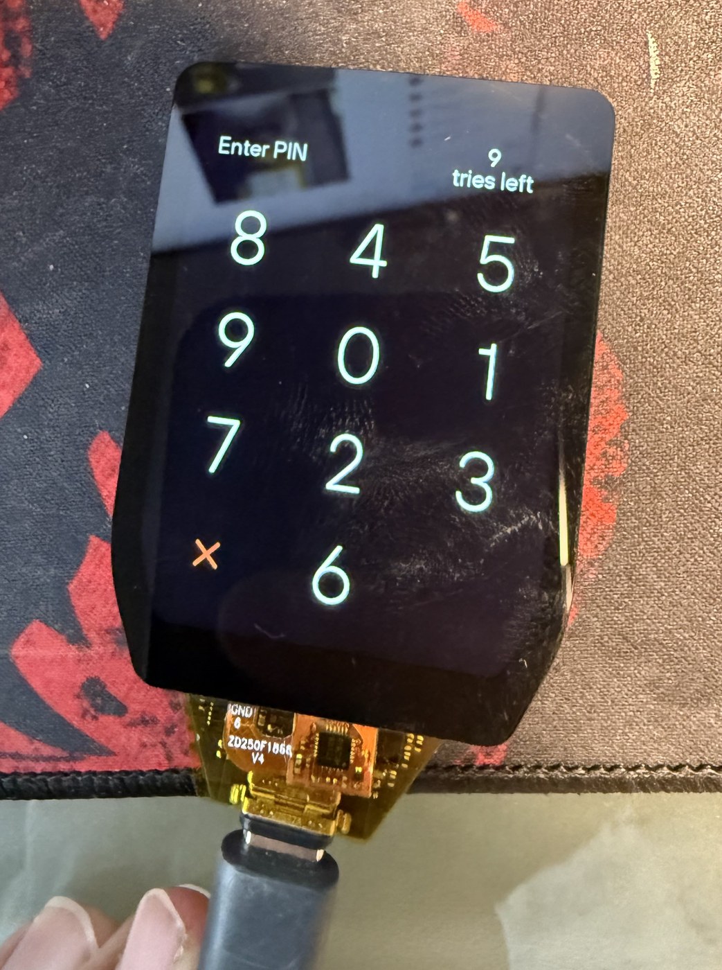 Trezor Safe 7 display and bare mainboard powered over USB-C outside the enclosure, showing the Enter PIN keypad
